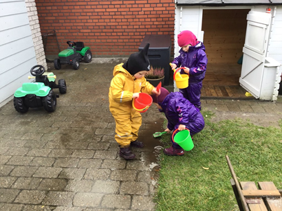 Leg i haven, tre børn undersøger en vandpyt med gummistøvler og skovle